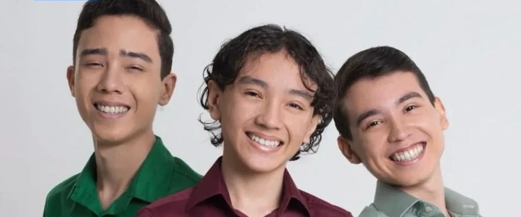 Imagem de três jovens componentes do grupo musical sorrindo.